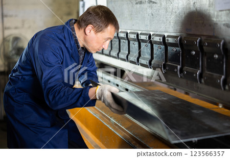 Adult man bends metal sheet under pressure Adult man bends metal sheet under pressure 123566357