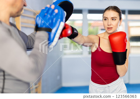 Athletic woman learns to box - hitting punch mitts. Woman with her trainer at gym 123566363