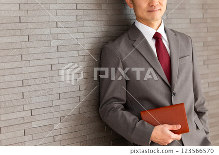 A middle-aged male businessman in a suit leaning against a wall and smiling 123566570