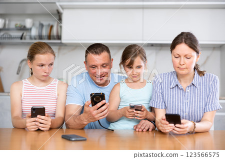 Teenage girls and parents sitting with smartphones at table in kitchen Teenage girls and parents sitting with smartphones at table in kitchen 123566575