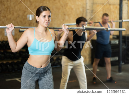 Motivated CrossFit female athlete lifting heavy body bar or barbell during group training in gym. Functional training concept. Motivated CrossFit female athlete lifting heavy body bar or barbell during group training in gym. Functional training concept. 123566581