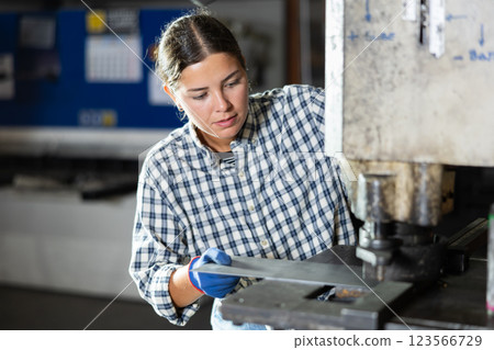 Young female worker operating punch press in metalworking workshop Young female worker operating punch press in metalworking workshop 123566729