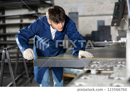 Young worker measuring metal sheet with tape measure in workshop Young worker measuring metal sheet with tape measure in workshop 123566760