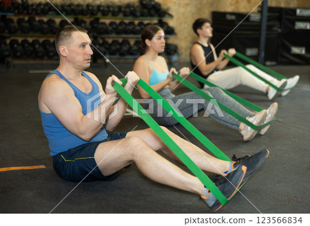 Active middle-aged man wearing sport clothes using resistance band during group workout in gym 123566834