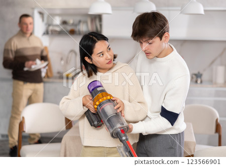 Young guy explains to girl how to use wireless vacuum cleaner Young guy explains to girl how to use wireless vacuum cleaner 123566901