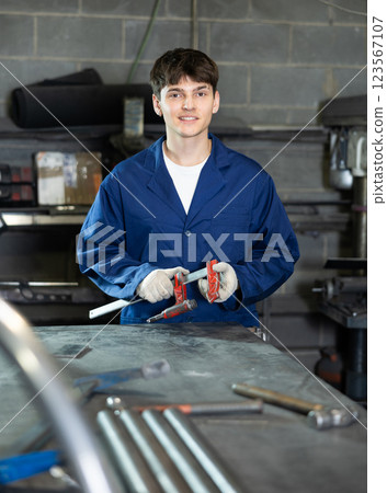 Young worker standing in metal workshop with clamping tool 123567107