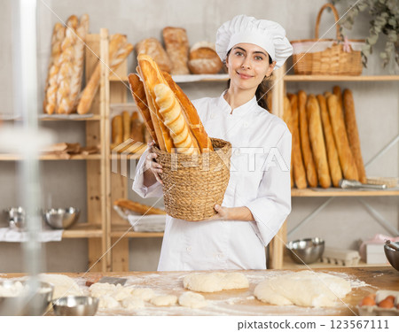 In working room of bakery, there is girl with baguettes in wicker basket in hands 123567111