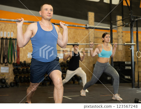 Energetic male athlete practicing sit-ups with rod near other people gym Energetic male athlete practicing sit-ups with rod near other people gym 123567248