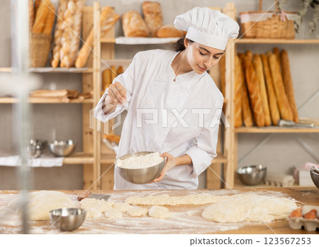 Young female baker sprinkling dough with flour 123567253