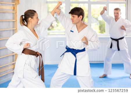 Woman and man in pairs exercising karate movements during group training in gym Woman and man in pairs exercising karate movements during group training in gym 123567259