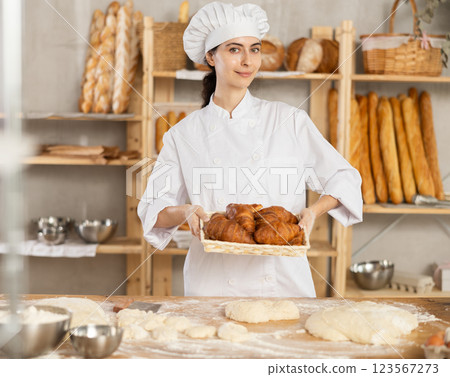 In working room of bakery, there is girl with croissants in wicker basket in hands 123567273