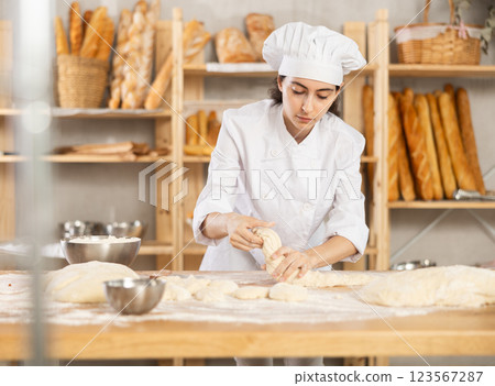 Young female baker kneading dough on table Young female baker kneading dough on table 123567287
