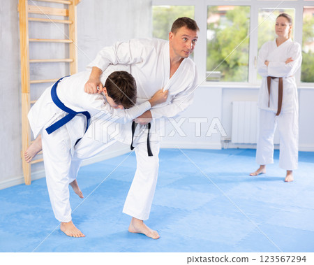 Judo or jiu-jitsu classes - two men practicing grabbing and throwing on sports mats under the guidance of trainer 123567294