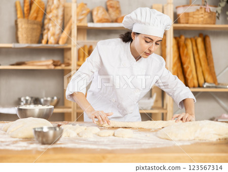 Young female baker kneading dough on table 123567314