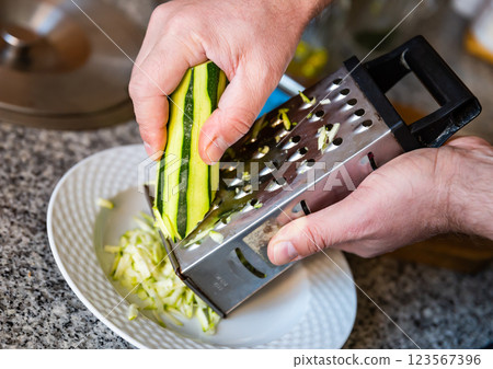 Hands rubs zucchini on grater close-up 123567396