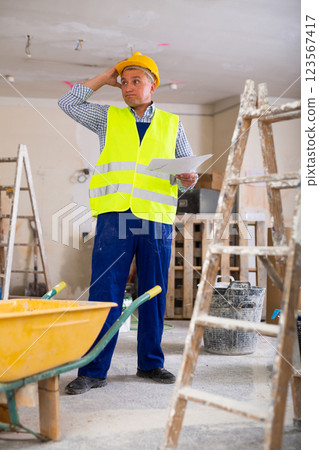 Frustrated worker in yellow vest and hard hat is dissatisfied with the way walls are plastered 123567417