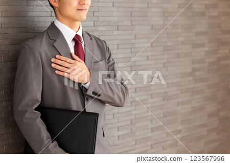 A middle-aged male businessman wearing a gray suit and holding his hand on his chest 123567996
