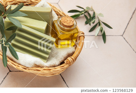 Olive soap bars, olive oil and branches resting in wicker basket on beige tile Olive soap bars, olive oil and branches resting in wicker basket on beige tile 123568129