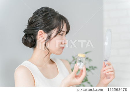 An Asian woman with a mirror suffering from rough skin and acne where vitamins and supplements do not work An Asian woman with a mirror suffering from rough skin and acne where vitamins and supplements do not work 123568478