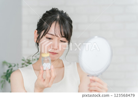一位有鏡子的亞洲女性皮膚粗糙和痤瘡,維生素和補品不起作用 一位有鏡子的亞洲女性皮膚粗糙和痤瘡,維生素和補品不起作用 123568479
