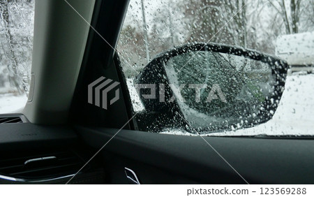 Drops On Wet Car Door Glass And Mirror Packed With Snow View From Inside Of Car On Street At Winter Day. Hot Air From Deflectors Melting Snow On A Car Parts  123569288