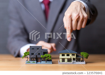 一位身著西裝的中年男性商人指著房屋模型 一位身著西裝的中年男性商人指著房屋模型 123570841