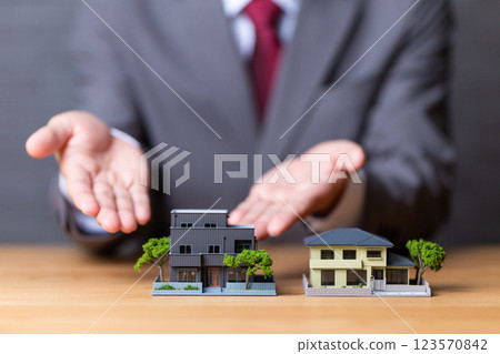 A middle-aged male businessman in a suit recommending a house model 123570842