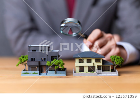 A middle-aged male businessman in a suit holding a house model and a magnifying glass 123571059