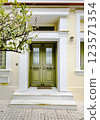 Beautiful entrance with green doors and decorative tree in front of a charming house 123571354