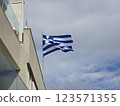 Greek flag proudly displayed on a building under cloudy skies in a coastal location 123571355