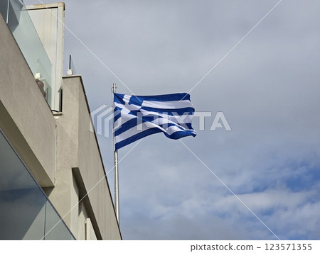 Greek flag proudly displayed on a building under cloudy skies in a coastal location 123571355