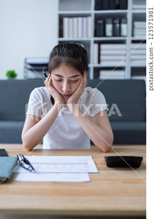 Stressed young woman in a setting reviewing documents at a table while finances and workload 123571981