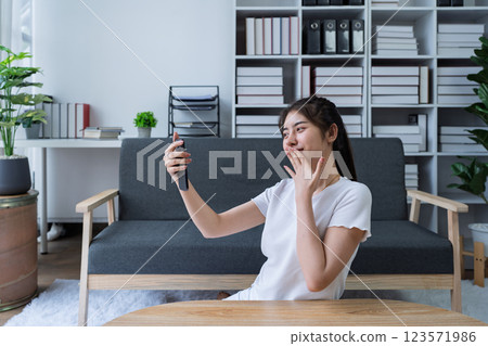 Young woman enjoying a video call on smartphone in modern living room with cozy decor and natural light 123571986