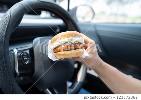 Asian lady holding hamburger to eat in car, dangerous and risk an accident. 123572362