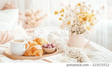 Morning breakfast spread featuring pastries, coffee, and flowers on a cozy bed during a soft light moment 123572512