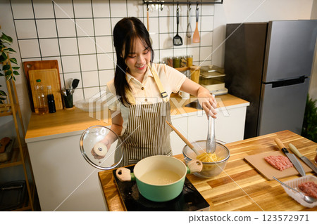 Smiling woman lifting boiled spaghetti from steaming pot while preparing a delicious homemade dish Smiling woman lifting boiled spaghetti from steaming pot while preparing a delicious homemade dish 123572971