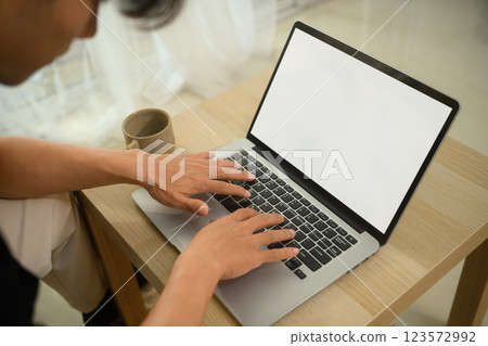 Close up young man using laptop on wooden coffee table at home Close up young man using laptop on wooden coffee table at home 123572992