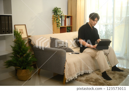 Handsome asian man browsing with digital tablet sitting on sofa in a living room 123573011