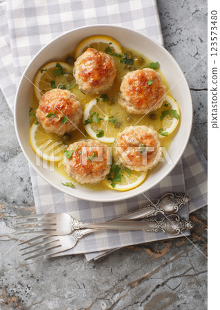 Chicken piccata meatballs with a delicious sauce of lemon, capers, white wine, and butter closeup in the plate. Vertical top view Chicken piccata meatballs with a delicious sauce of lemon, capers, white wine, and butter closeup in the plate. Vertical top view 123573480