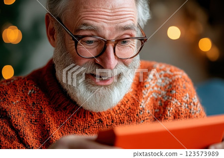 Surprised middle aged man opens mysterious gift box in a bright and warm room 123573989