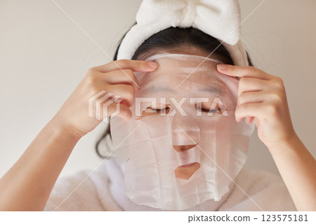 A teenage woman applying a sheet mask to her face after a bath at home 123575181