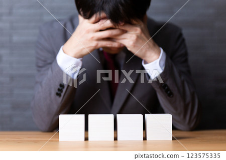 Four white wooden blocks and a worried middle-aged male businessman Four white wooden blocks and a worried middle-aged male businessman 123575335