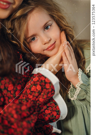 Mom gently hugs her little beautiful daughter in a green dress. 123575364