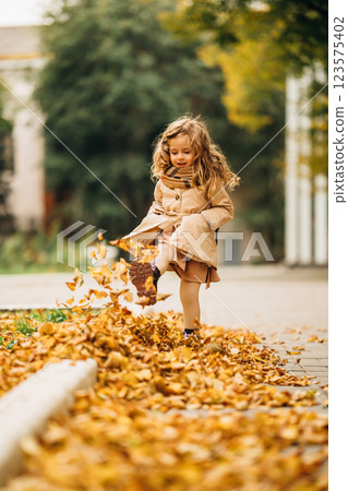 Little girl enjoys playing in a pile of autumn leaves on a sunny day 123575402