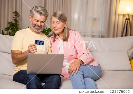Contented mature couple doing online shopping and looking involved Contented mature couple doing online shopping and looking involved 123576065