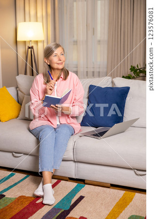 Positive mature woman in pink sitting on a sofa with a laptop Positive mature woman in pink sitting on a sofa with a laptop 123576081