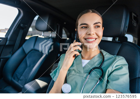 Young woman in scrub suit sitting in a car and talking on the phone Young woman in scrub suit sitting in a car and talking on the phone 123576595