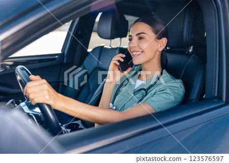 Young woman in scrub suit sitting in a car and talking on the phone 123576597
