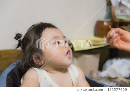 [Baby with tied hair eating baby food] 123577639