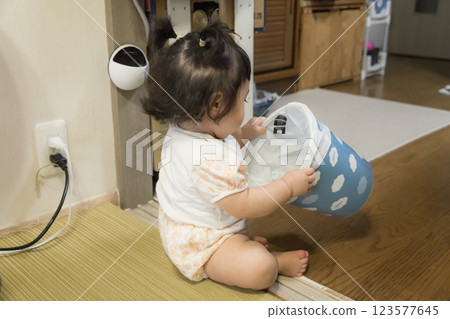 [Pigtailed baby playing with a trash can] 123577645